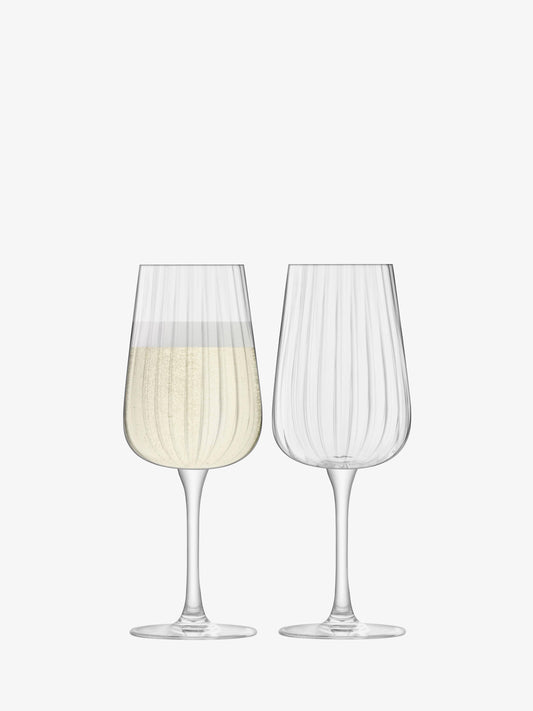 Two flute glasses with one containing a white beverage on a white background