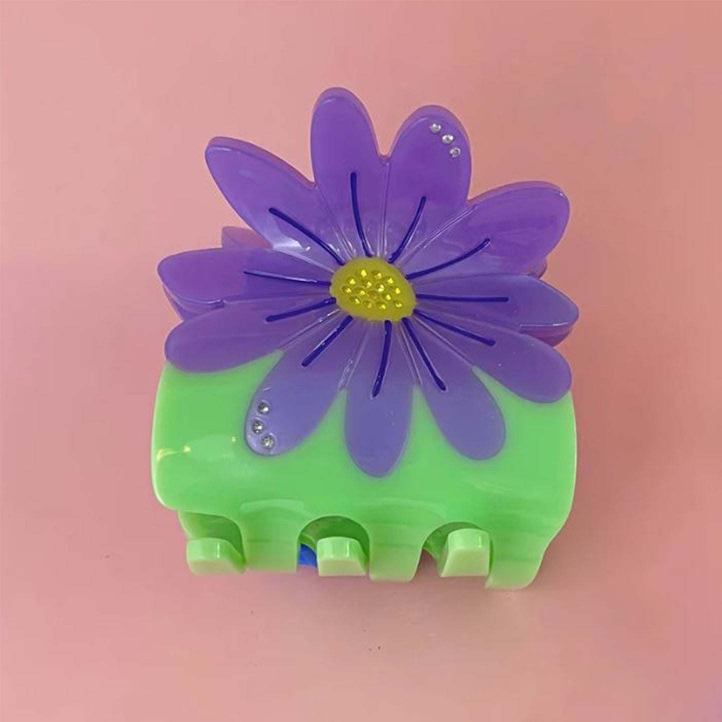 green claw clip with large purple daisy on a pink background