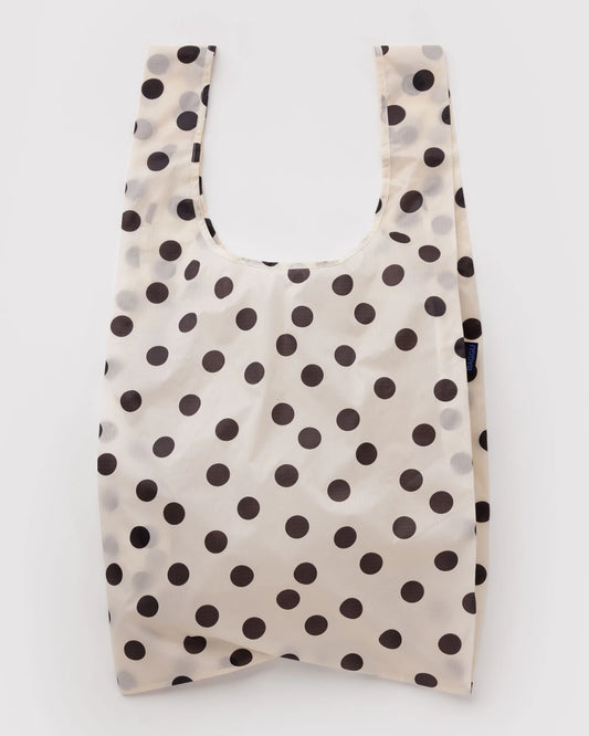 A reusable plastic shopping bag with a black polka dot pattern on a warm off-white background, shown against a plain white studio background.