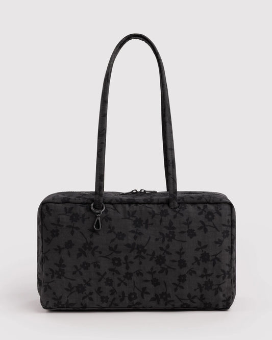 A black rectangular handbag with a subtle tonal floral pattern, featuring two long shoulder straps and a top zipper closure, set against a plain light gray background.