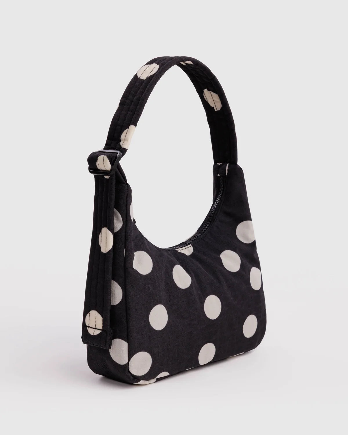 A black shoulder bag with large white polka dots, featuring a single top handle and an adjustable shoulder strap, shown against a light gray background.
