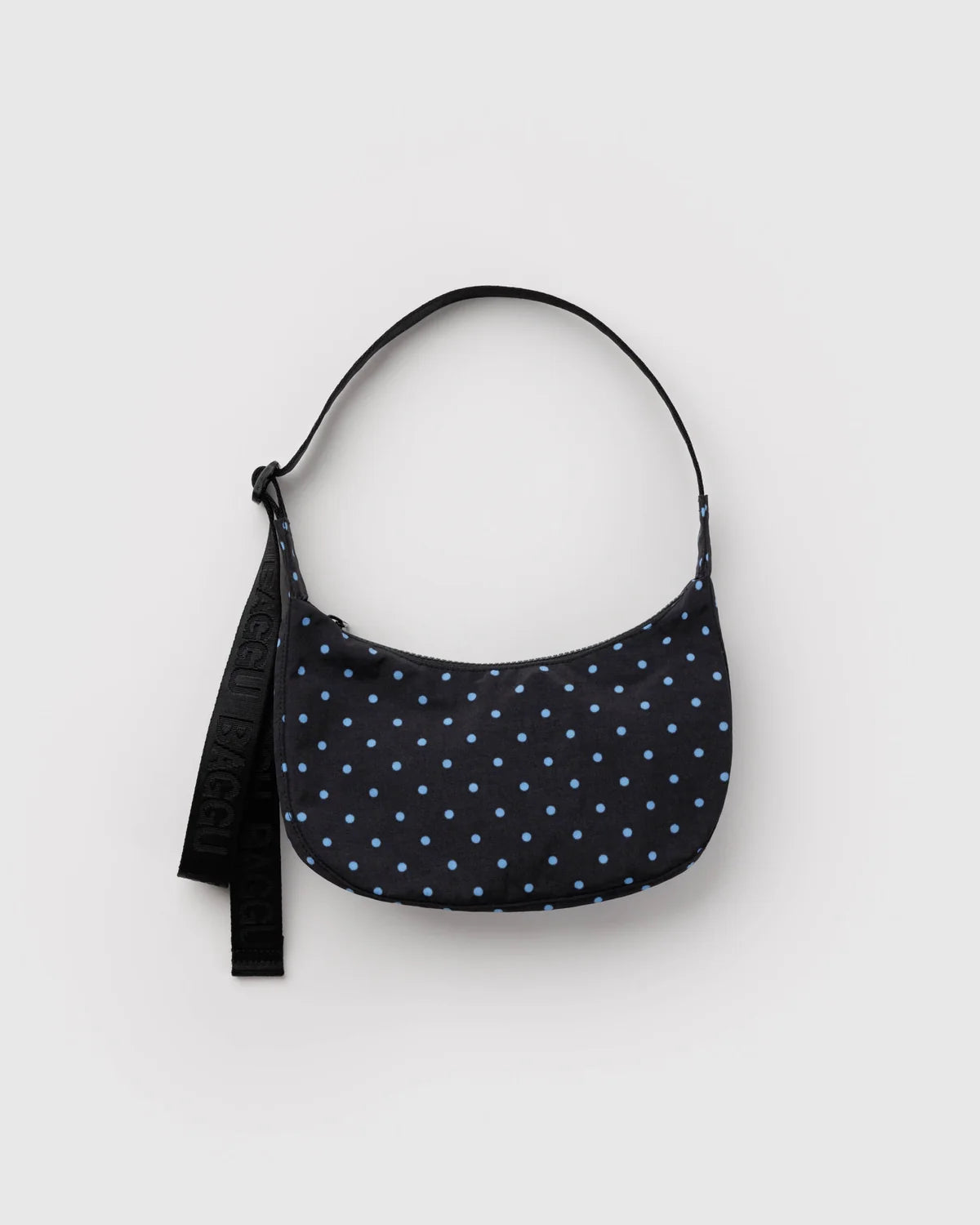 A crescent-shaped shoulder bag in black with a light blue polka dot pattern, featuring a black adjustable strap with white lettering, photographed on a light gray background.