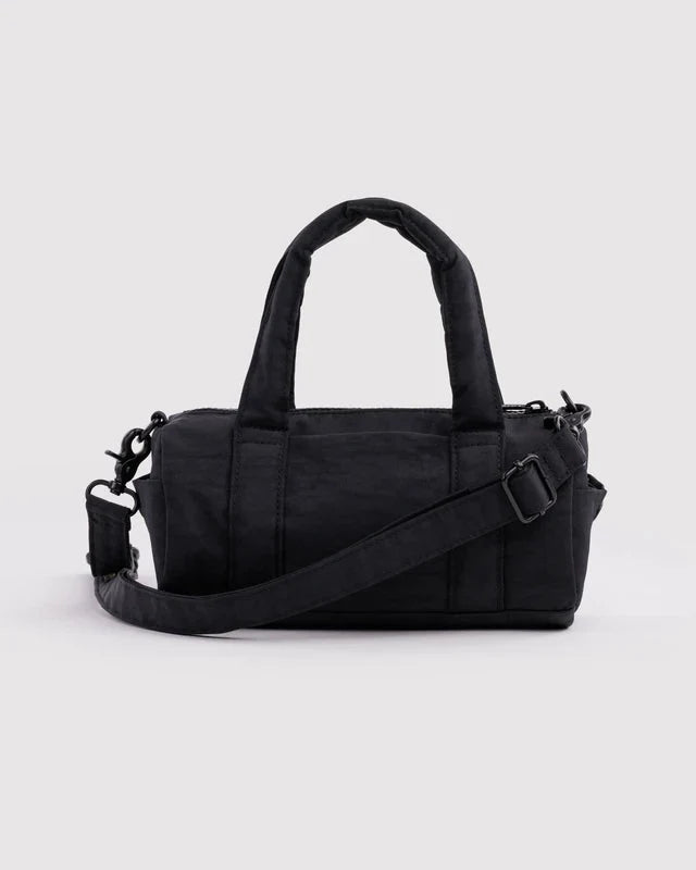 A black nylon duffel bag with dual top handles and an adjustable shoulder strap, photographed against a light gray studio background.