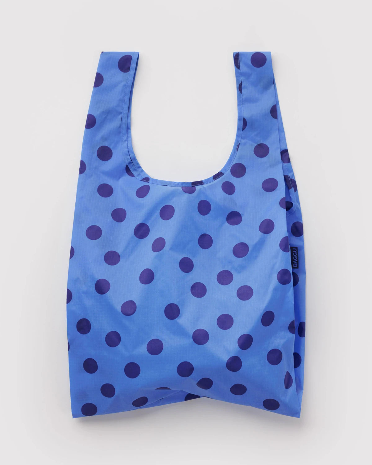 A reusable blue shopping bag with a dark blue polka dot pattern, shown flat against a light gray background.