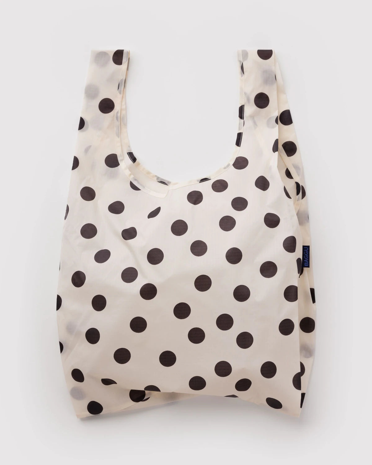 A reusable folding shopping bag with a cream background and dark brown polka dots, shown against a plain light gray background.