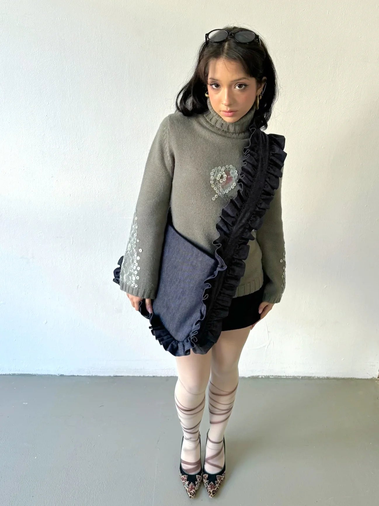 Person wearing a gray sweater with ruffled details and a skirt against a white background