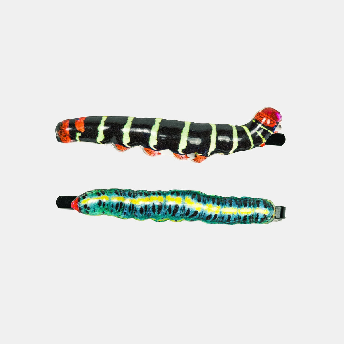 Two colorful caterpillar-themed hair claw clips on a light gray background. The top clip is black with lime green stripes and orange feet, while the bottom clip is blue with yellow stripes and red accents.