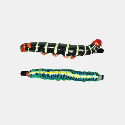 Two colorful caterpillar-themed hair claw clips on a light gray background. The top clip is black with lime green stripes and orange feet, while the bottom clip is blue with yellow stripes and red accents.