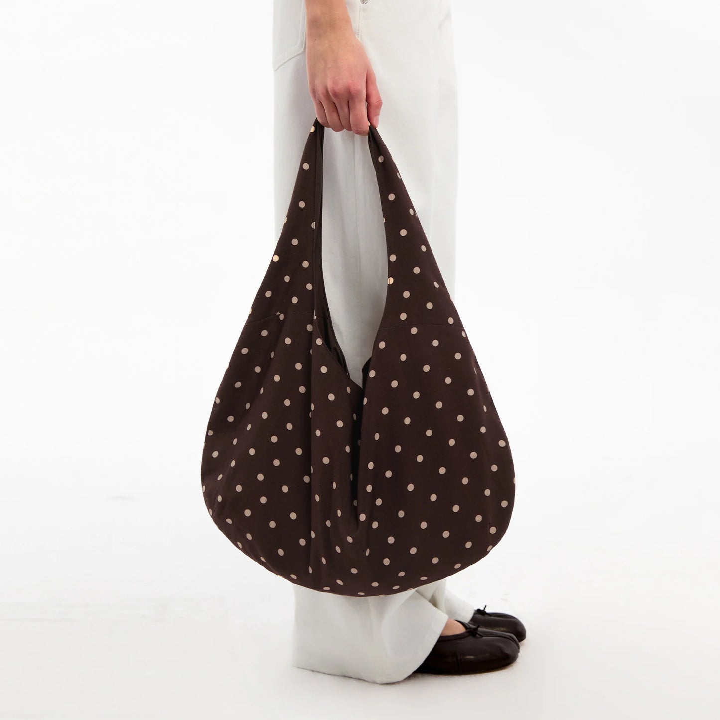 Brown polka dot bag held by a person on a white background