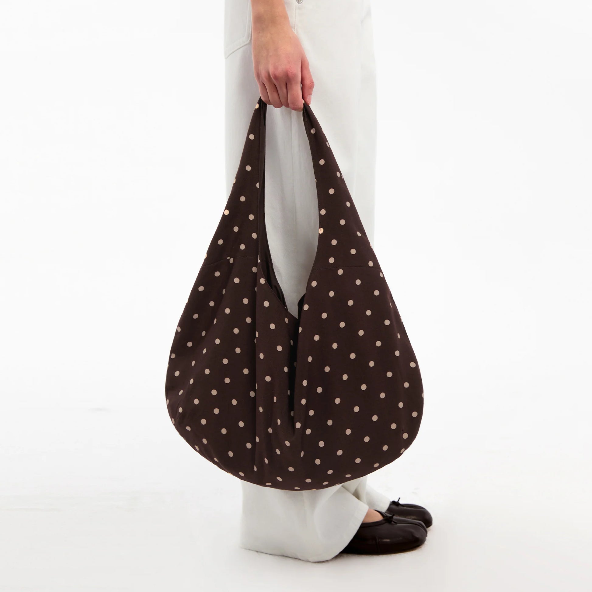 Brown polka dot bag held by a person on a white background