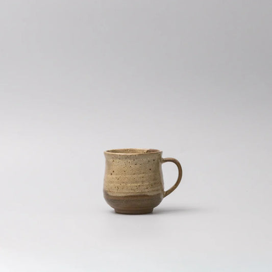 A small handmade ceramic mug with a textured, speckled glaze in earthy beige and brown tones, featuring a simple C-shaped handle, set against a plain light gray background.