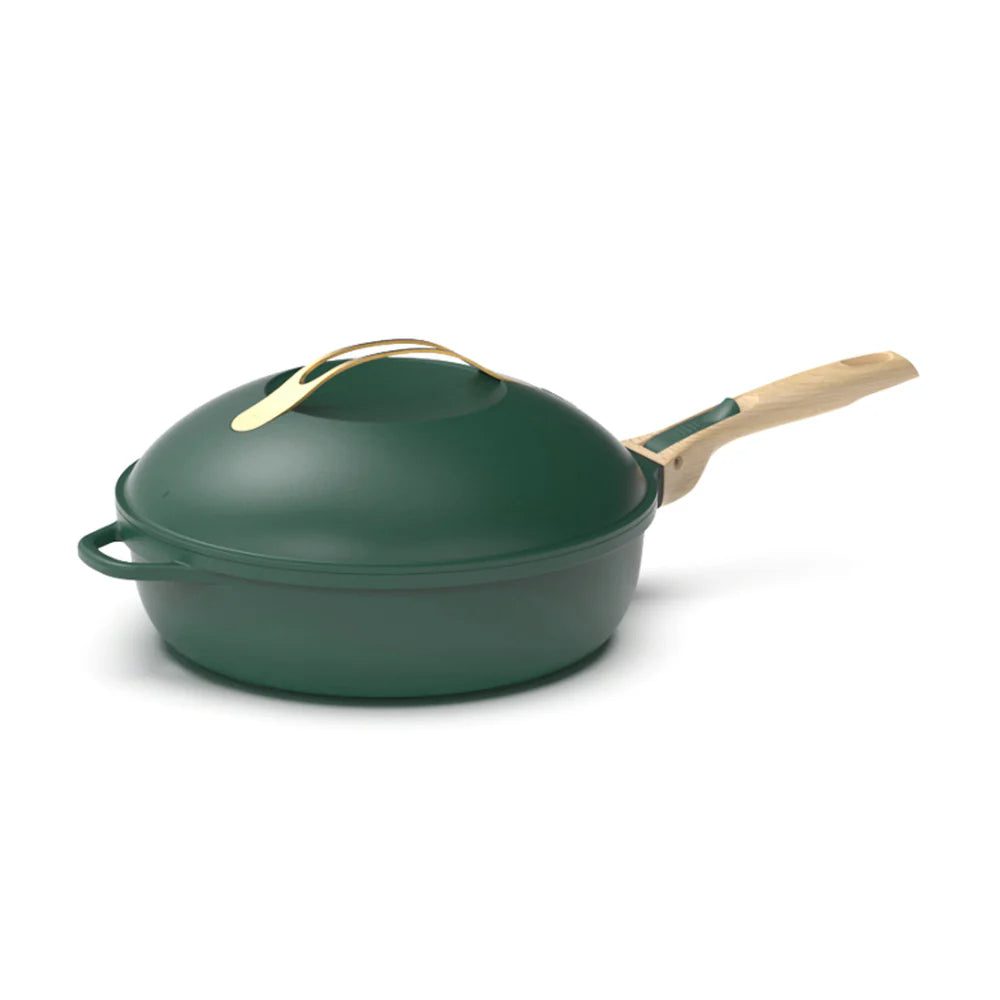 A dark green Cookut The Fabulous Pan with a lid and wooden spatula, featuring gold-colored handles.