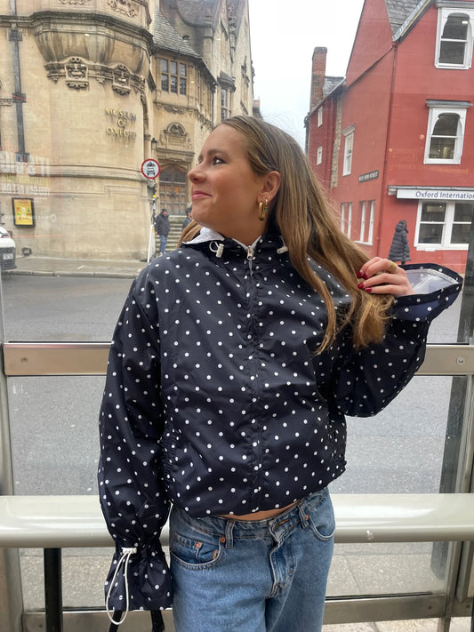 Woman wearing a navypolka dot jacket with long sleeves in an urban setting.
