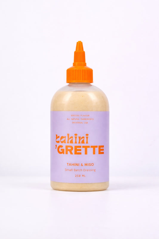Bottle of Tahini Grette with a purple label and orange cap on a white background