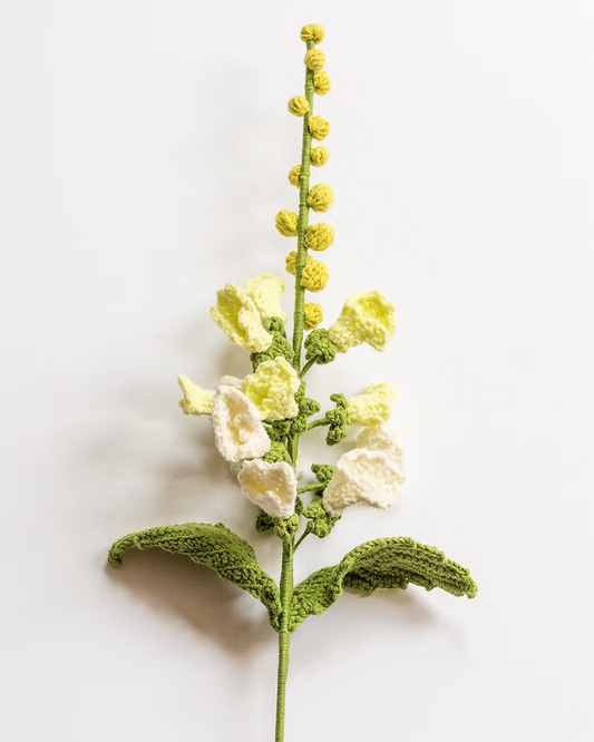 A crocheted artificial flower stem featuring pale yellow and off-white blossoms with textured green leaves, displayed against a clean white background.