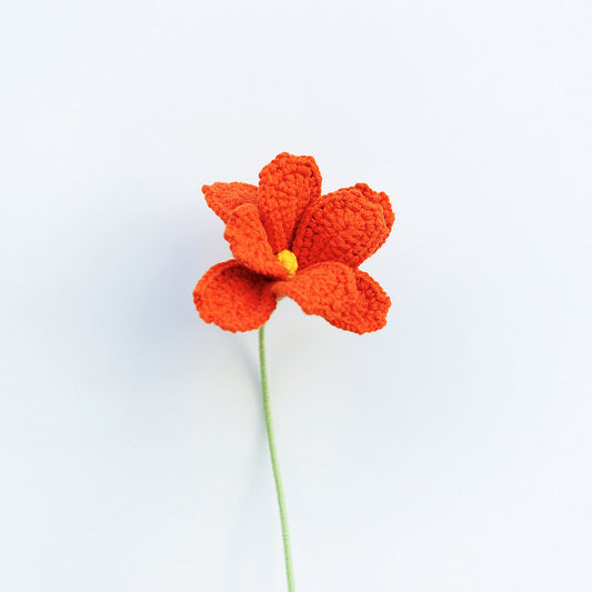 Crocheted orange flower with a yellow center on a white background
