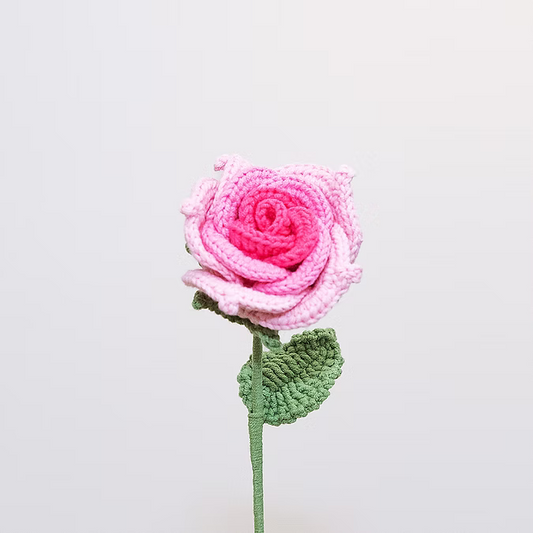 Crocheted pink rose with a green stem on a light gray background