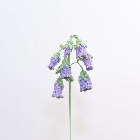 Knitted purple flowers with green leaves on a light pink background