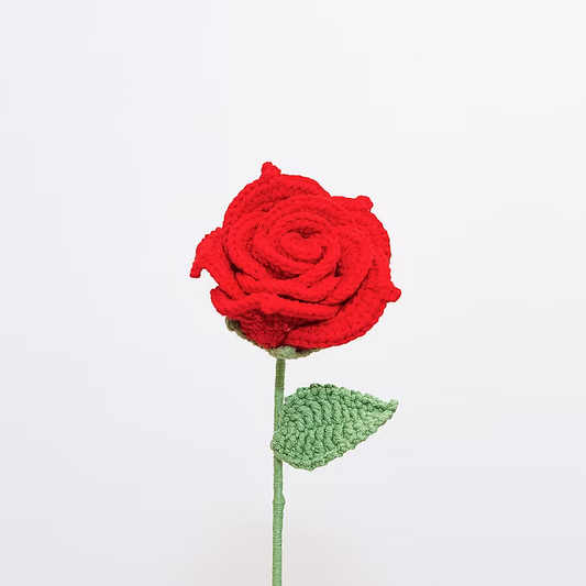 Crocheted red rose with a green stem and leaf on a white background