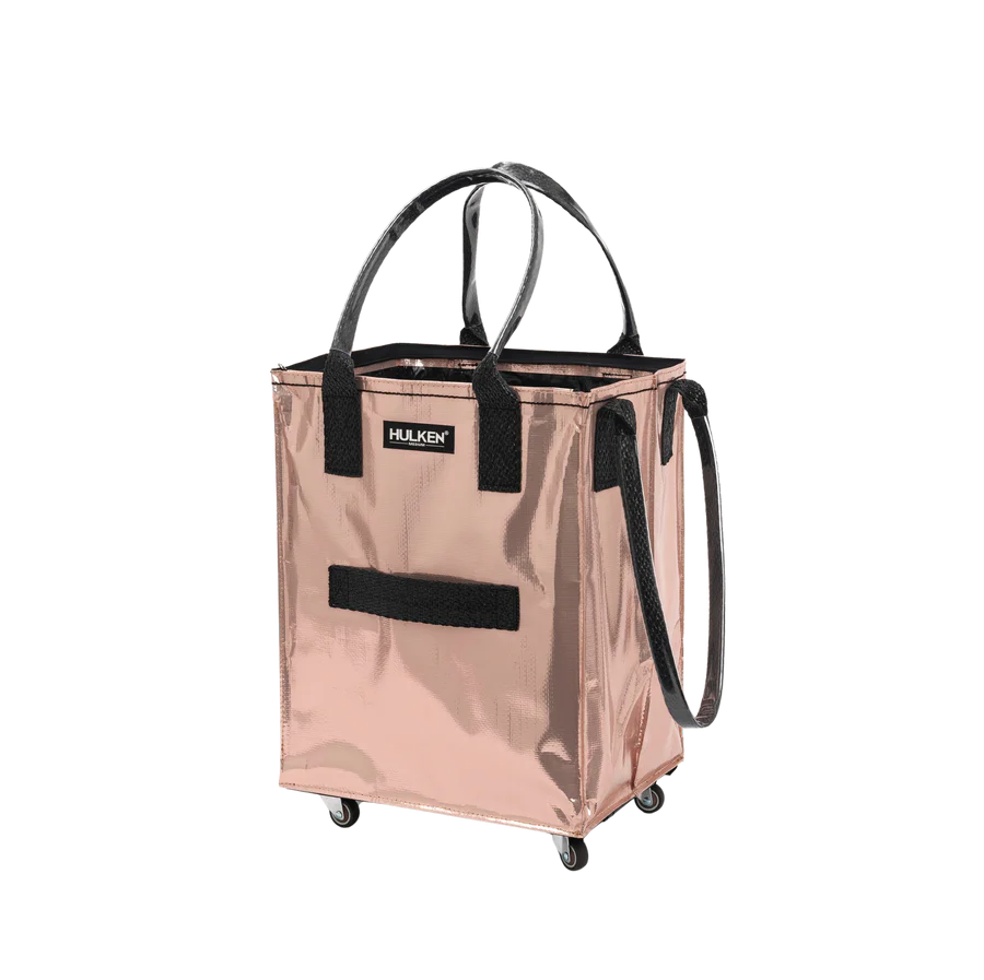 A metallic rose gold HULKEN rolling utility tote bag with black handles, a black front strap, and black wheels, shown on a plain white background.