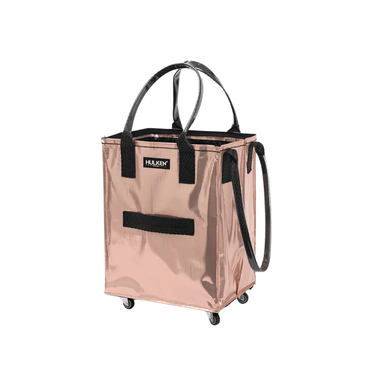 A metallic rose gold HULKEN rolling utility tote bag with black handles, a black front strap, and black wheels, shown on a plain white background.