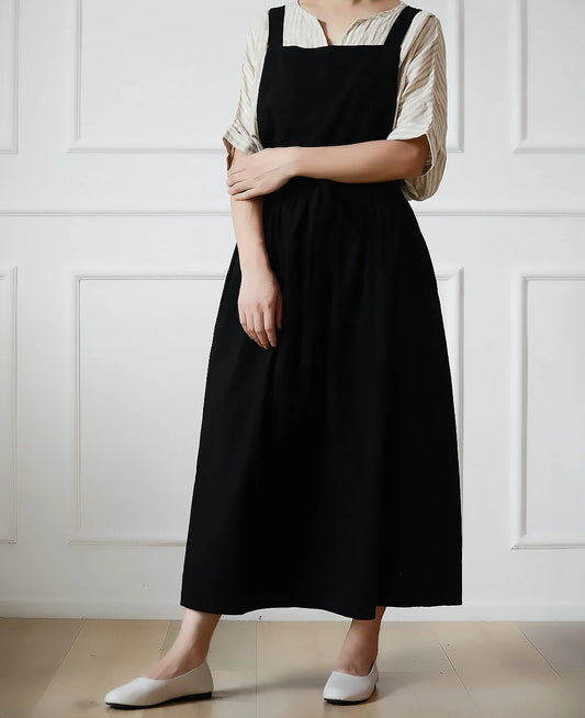 Person wearing a black apron over a white shirt against a white paneled wall.