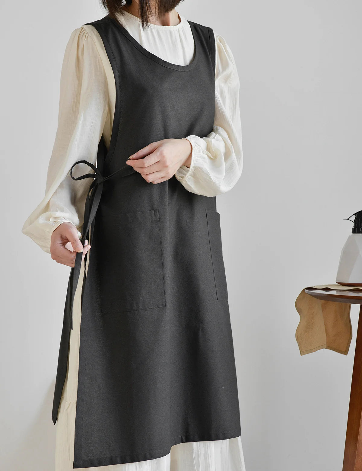 Person wearing a black apron over a white outfit on a plain background