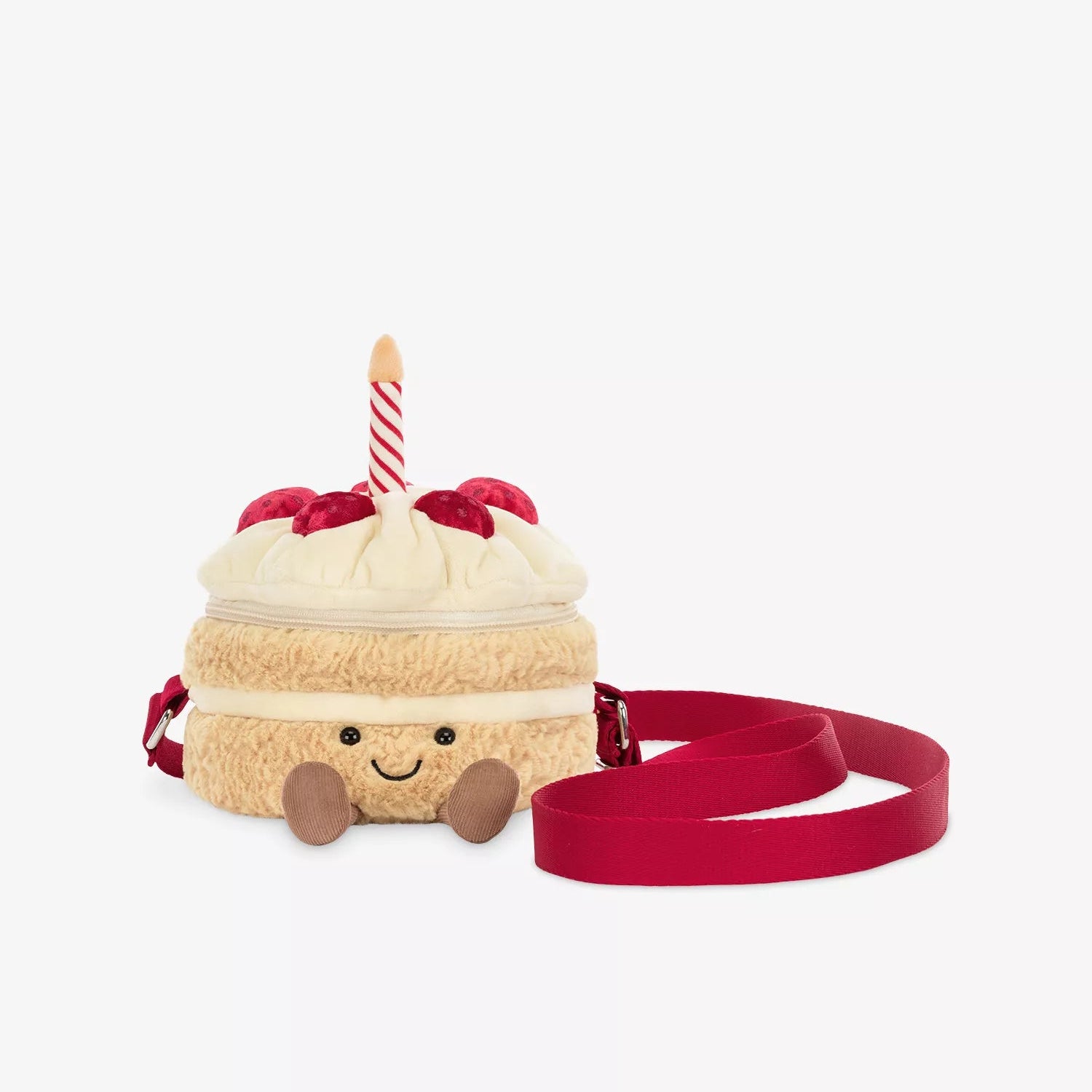 A plush cake-shaped crossbody bag with a cream-colored frosting top, red cherries, a red-and-white striped candle, and a red strap, shown on a light gray background.