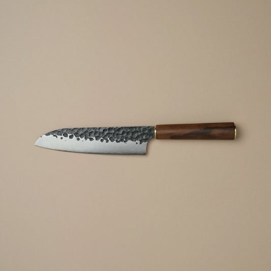 A Japanese-style kitchen knife with a hammered steel blade and a dark brown wooden handle, shown horizontally against a solid beige background.