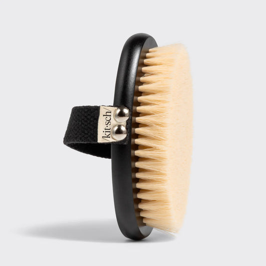 Body brush with black handle and wooden bristles on a light gray background