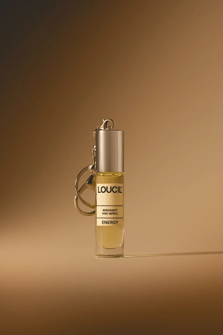 A small cylindrical perfume or fragrance bottle with a metallic silver cap and keychain ring, containing a pale yellow liquid. 
