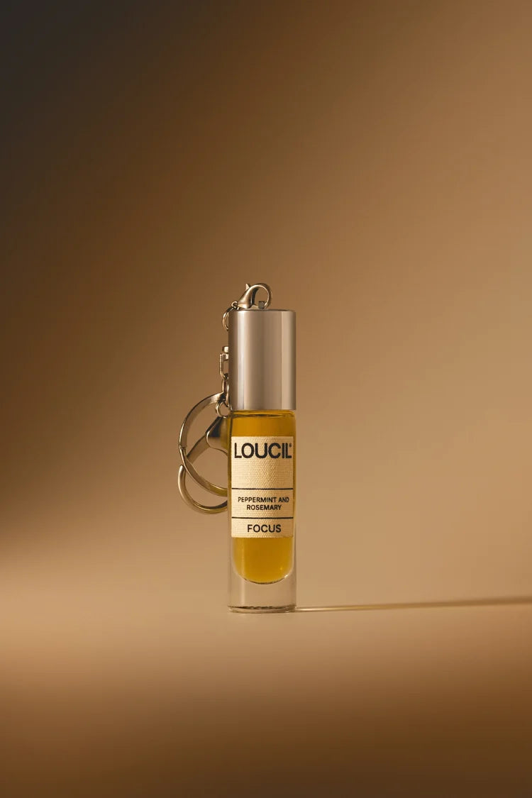 A small cylindrical perfume or fragrance roller bottle with a silver cap and keychain ring, filled with amber-yellow liquid. 