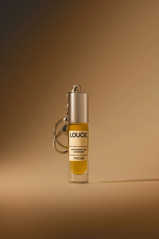 A small cylindrical perfume or fragrance roller bottle with a silver cap and keychain ring, filled with amber-yellow liquid. 