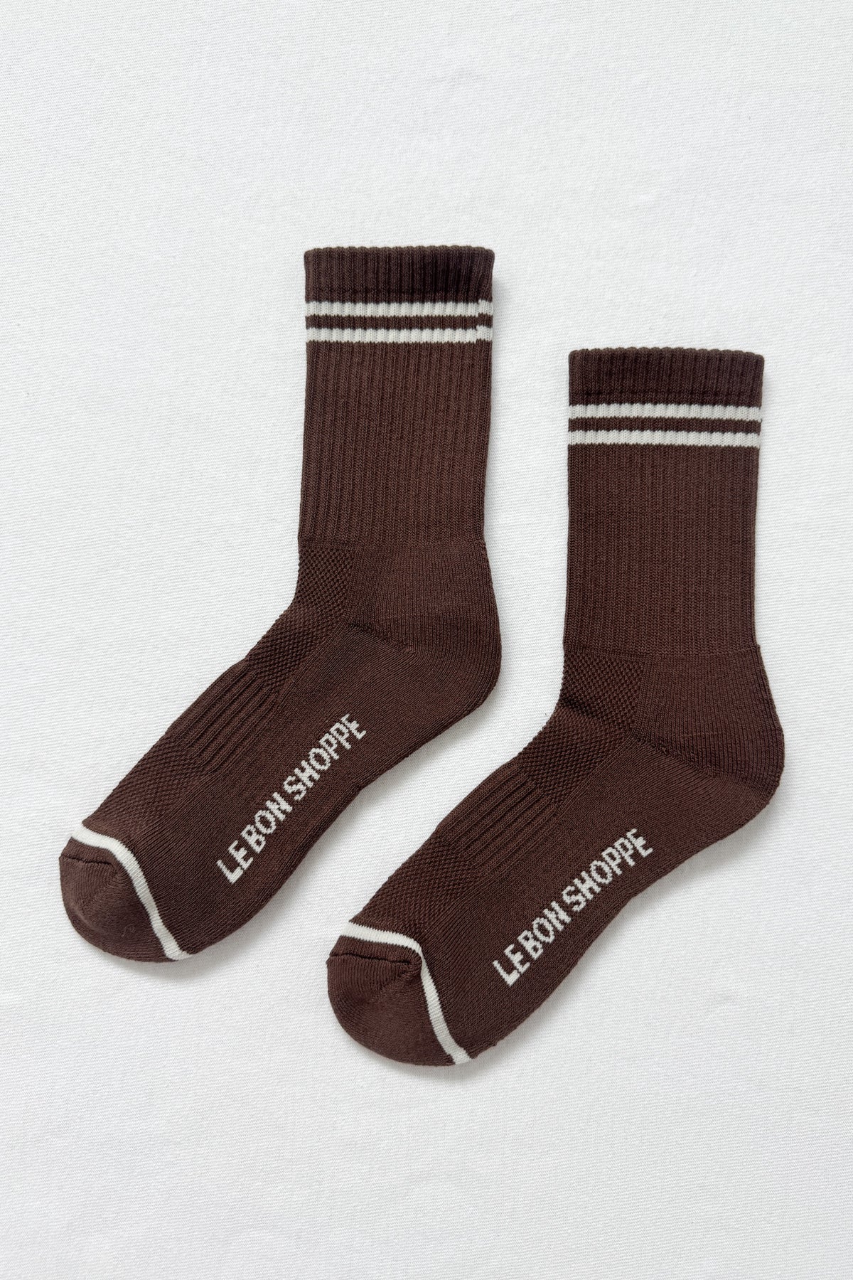 Pair of brown socks with white stripes and 'Le Bon Shoppe' branding on a light gray background
