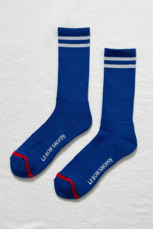 Pair of blue socks with white stripes and red accents on a light gray background