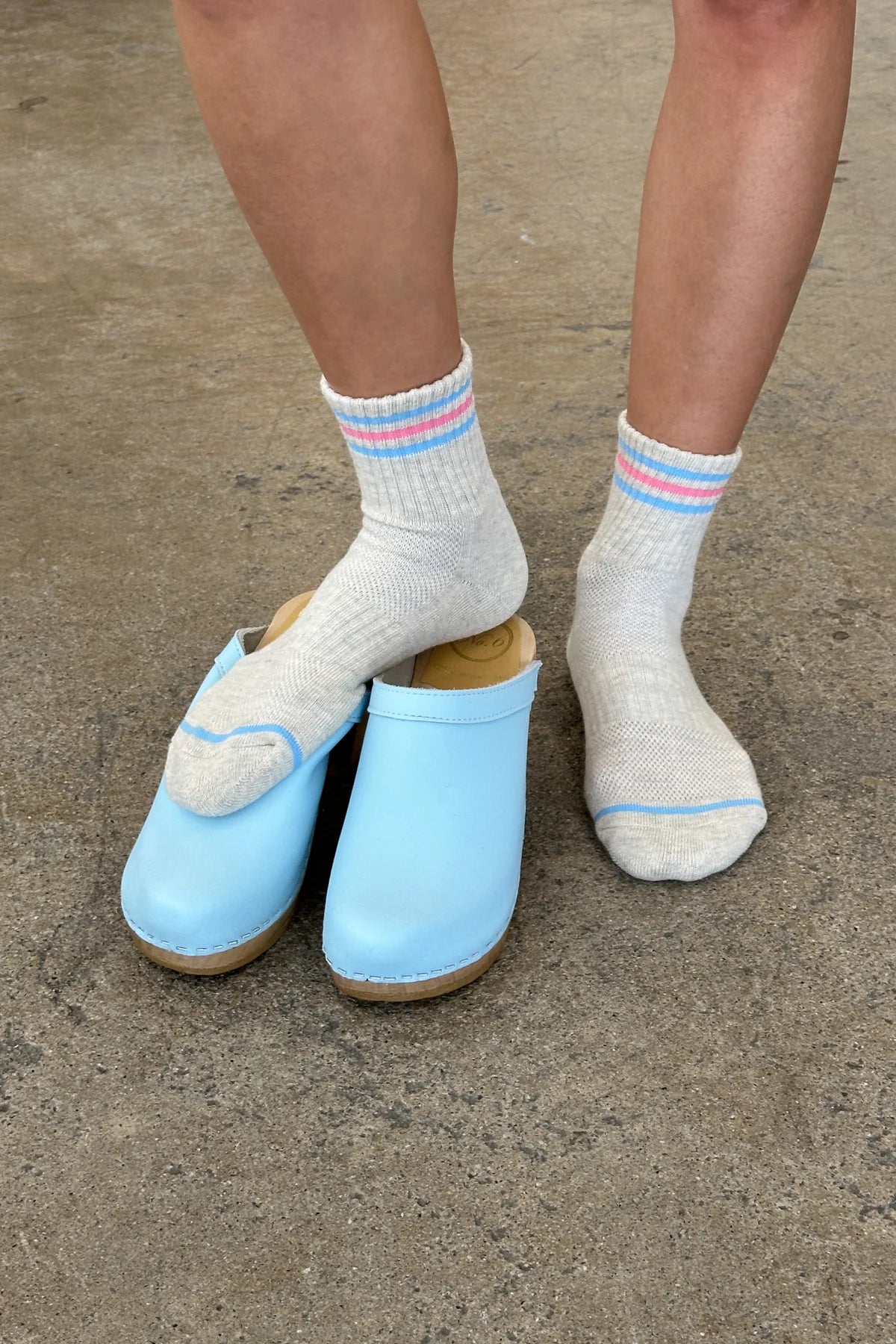 Light blue clogs worn with white socks on a concrete floor