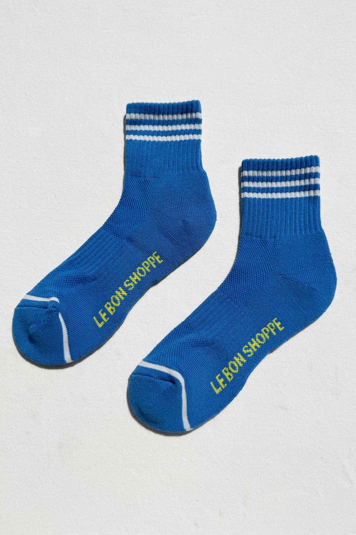 Pair of blue socks with white stripes and 'LE BON SHOPPE' branding on a light gray background