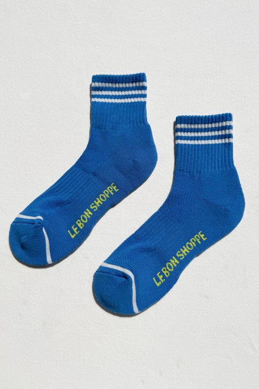 Pair of blue socks with white stripes and 'LE BON SHOPPE' branding on a light gray background