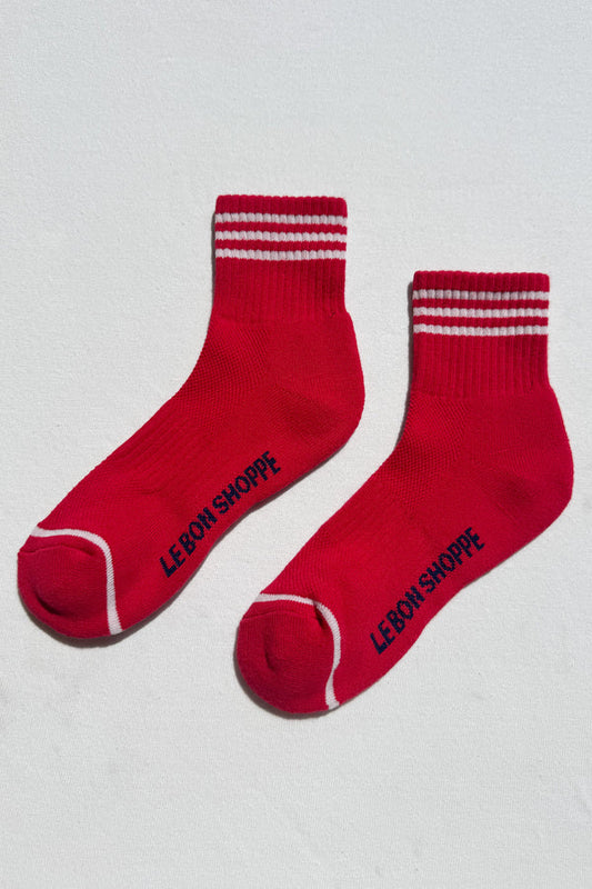 Red socks with white stripes and 'Le Bon Shoppe' branding on a light gray background