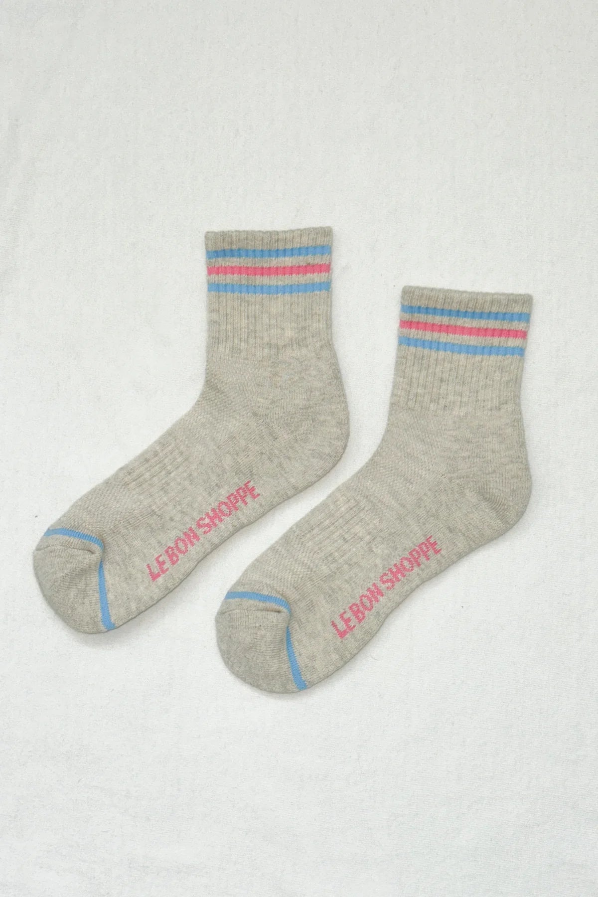 Gray socks with colorful stripes and 'Le Bon Shoppe' branding on a light gray background