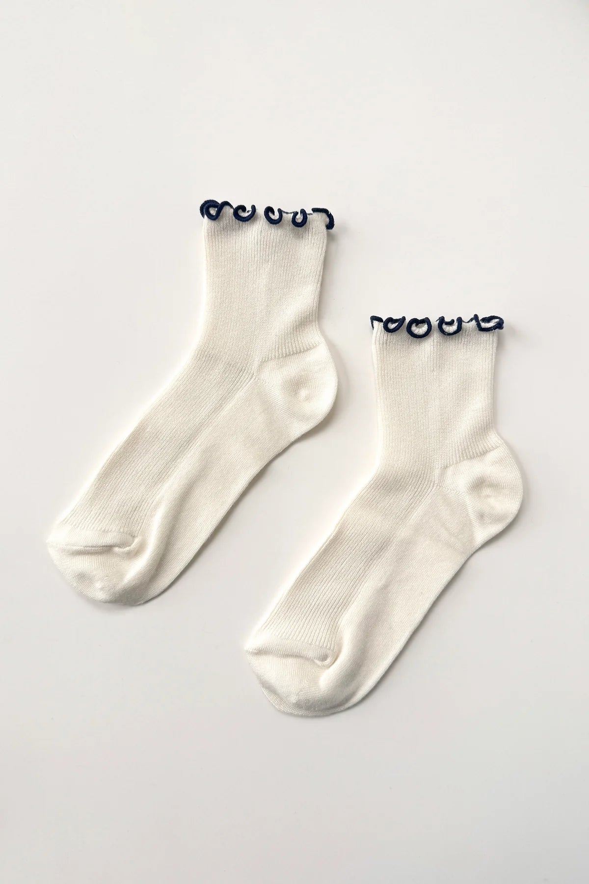 Pair of white socks with black lettuce frill on a light gray background