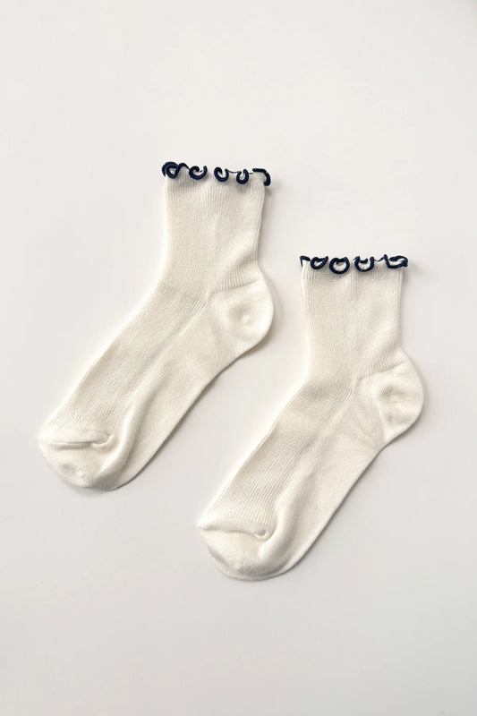 Pair of white socks with black lettuce frill on a light gray background