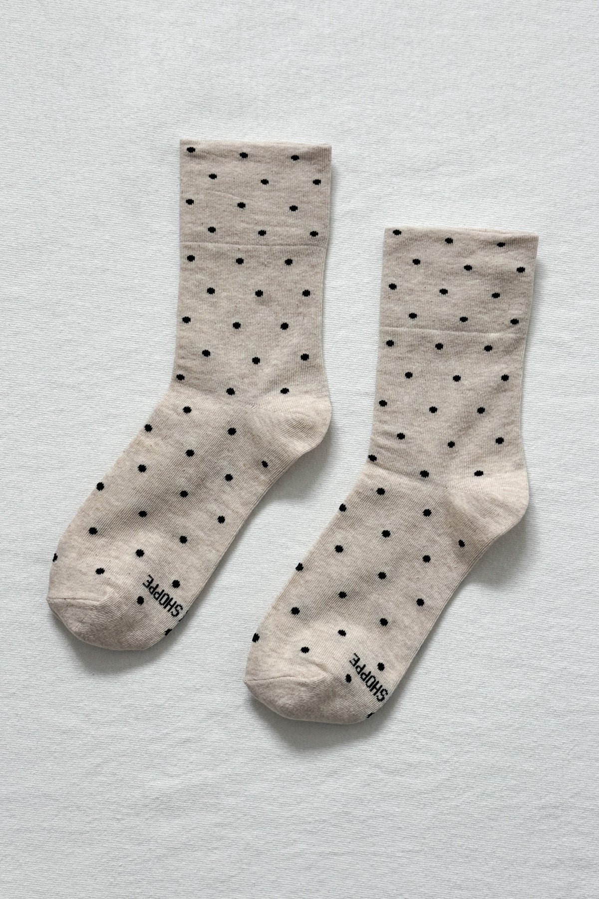 Pair of beige socks with black polka dots on a light gray background