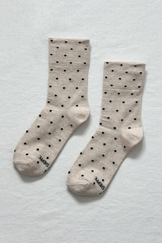 Pair of beige socks with black polka dots on a light gray background