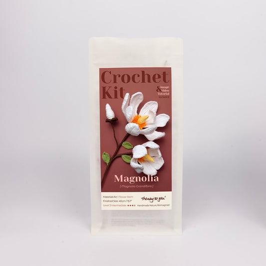 Crochet kit packaging with magnolia flower design on a gray background