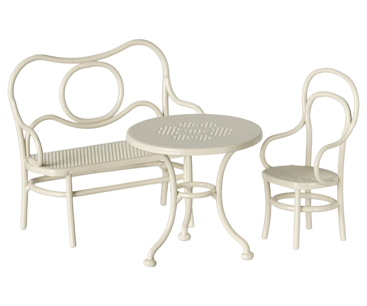 A three-piece outdoor patio bistro set in a cream or off-white finish, including a curved bench with a slatted seat, a matching armchair, and a small round table with a slatted top.