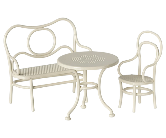 A three-piece outdoor patio bistro set in a cream or off-white finish, including a curved bench with a slatted seat, a matching armchair, and a small round table with a slatted top.