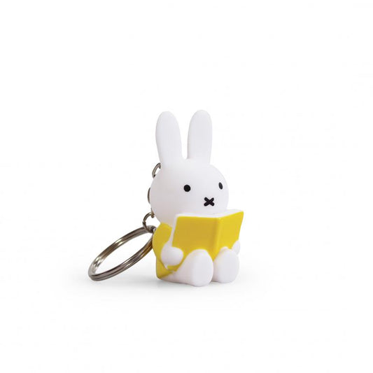 Keychain of a white rabbit character reading a yellow book on a white background