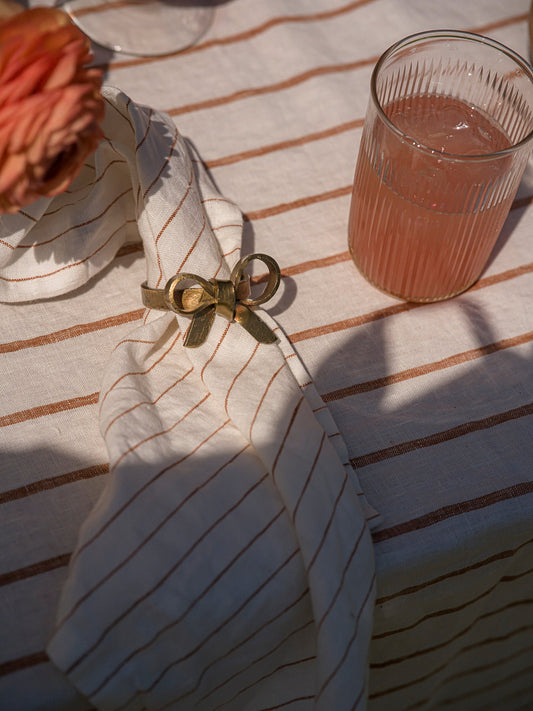 Glass of pink drink on a striped tablecloth with a decorative napkin.