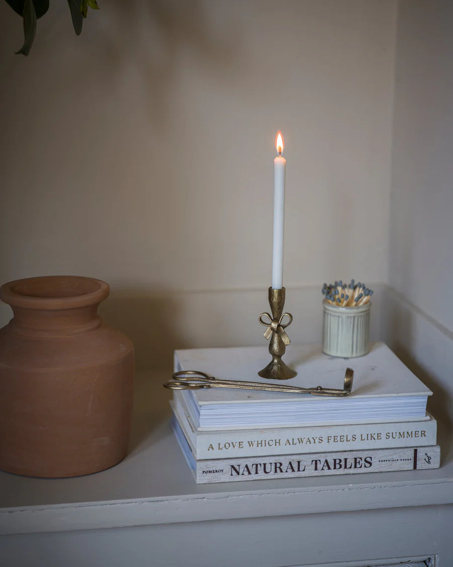 Candle on a stack of books with a vase and small container in the background